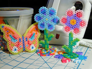 Figures of a butterfly and two flowers made from fuse beads.
