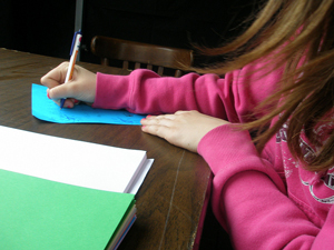 Photo of a girl's hands and part of a desk as she composes a letter