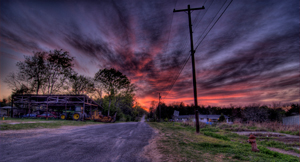A photograph of a sunset in rural Alabama. There are some agricultural buildings and a house in the background.