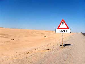 photo of a sand and desert as far as the eye can see with a sign in the foreground that reads “Sand”