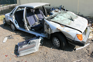 A photograph of a car that has been in an accident. The front end is crumpled up, all of the glass is gone, and the doors have been removed.