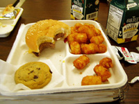 Photo of a half-eaten school lunch consisting of a burger, tater tots, and a chocolate chip cookie