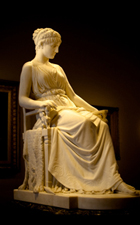 A marble statue of Penelope. She is sitting in a tall chair, dressed elegantly in a flowing dress, looking sadly downward.