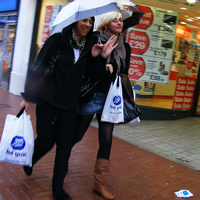 A photograph of two women walking down a city street sharing an umbrella