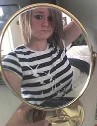 A photograph of a teenage girl looking at herself in the mirror.