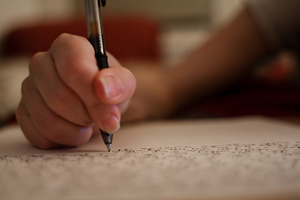 A photograph of a person's hand using a pen to write on a piece of paper