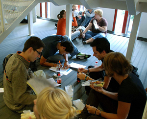 A photograph of students sitting in a group on the floor eating and studying