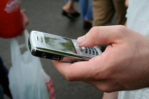 A photograph of a person's hand holding a mobile phone, texting with their thumb