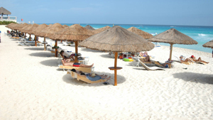 A photograph of rows of thatched beach umbrellas on a beach