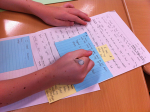 A photograph of a student revising a paper using note cards and post it notes. The student is holding a pen.
