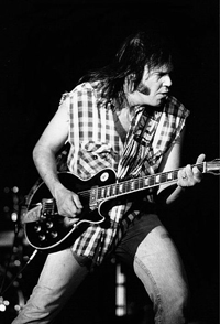 A photograph of musician songwriter Neil Young performing. He is playing a guitar.