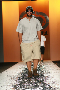 A male model modeling summer wear; a t shirt, shorts, and a baseball hat.