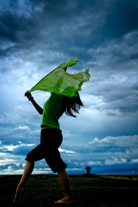 A photograph of a woman dancing under an evening sky.