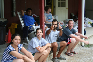 = A photograph of several camp counselors, male and female, seated outside of a cabin