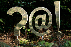 A photograph of an outdoor sculpture featuring several punctuation marks; a question mark, an 'at' symbol, and an exclamation point.