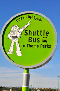 A photograph of a sign that indicates that the shuttle bus to theme parks stops here. There is picture of Buzz Lightyear from Toy Story on the sign.