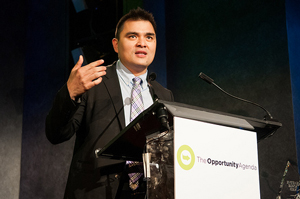 A photograph of Jose Antonio Vargas giving a speech. He is wearing business attire, and standing behind a podium.