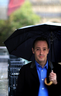 Author David Sedaris walking under an umbrella in the rain