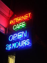 Neon sign on side of building with words “Internet Cafe Open 24 Hours”