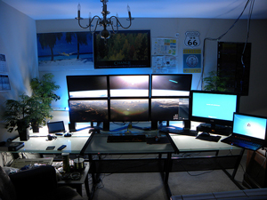 A desk with an array of monitors. The cluster of six computer screens shows the smooth curve of the earth.