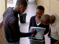 A photo of three African American students working on a tablet computer in the hall of a school building