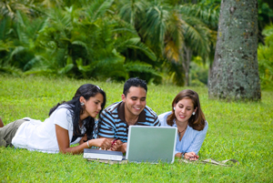 Three teenagers looking at a laptop in a grassy field