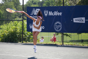 A woman’s tennis game. The photograph shows a player appearing to hang in the air as she jumps to return a shot. A banner behind her advertises several local businesses and a few software companies.