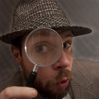 A bearded dressed as Sherlock Holmes peers through a magnifying glass at the camera.