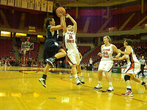 A woman's basketball game. Two of the athletes seem to hang in the air as they both leap for the basketball