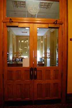 Photo of two big wooden doors with large glass panes on which is written “The Office of the Principal”