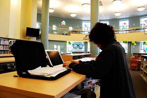 A photograph of female student working on a laptop computer in a library.