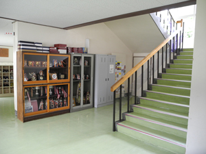 A photograph of a stairwell in a school. Next to the stairs is a trophy case and several lockers.