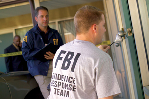A photograph of two FBI officers at a crime scene. One of them has a t-shirt that indicates that he is an Evidence Response Team member.