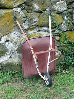 Image of a red wheelbarrow leaning against a stone wall