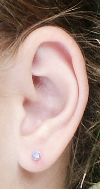 A photograph of a woman's ear with a stud earring in the lobe
