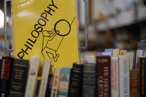 = A photograph of a sign in a library that reads, 'philosophy.' It has a drawing of a person pushing a rock up a steep hill.