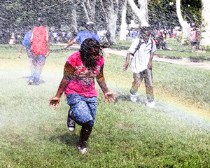 A photograph of children running through a sprinkler in a park