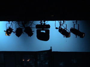 A photograph of stage lights silhouetted against a dimly lit screen