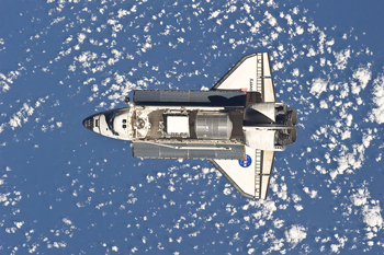 A photograph of the space shuttle Discovery taken in space flight from above; The shuttle's cargo bay doors are open.