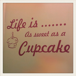 A photograph of a sign that reads, “Life is as sweet as a cupcake”