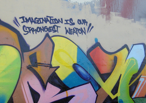 A photograph of graffiti art on a wall. Above the art is the phrase, 'imagination is our strongest weapon.'