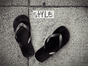 A photograph of a pair of flip flops on a sidewalk with the word 'style' between them