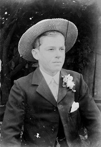 A late 19th century photograph of a young man wearing a suit with a flower in his lapel. He is also wearing a boater hat.