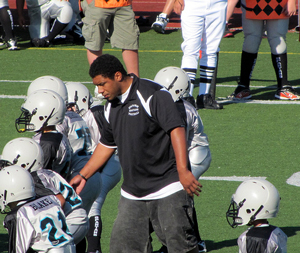 photo of a middle school coach who is coaching suited-up players from behind the line of scrimmage