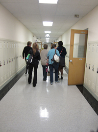 A photograph of five students walking down a school hallway lined with lockers