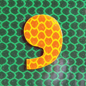 An artistic rendering of a comma that’s orange with a yellow pattern that resembles a chain-link fence
