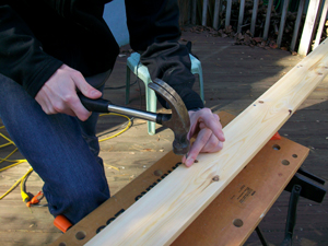 A photograph of a person hammering a nail into a board on a saw horse.