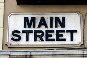 A photograph of a Main Street sign. It is a carved wood sign that is on a wall of a building.