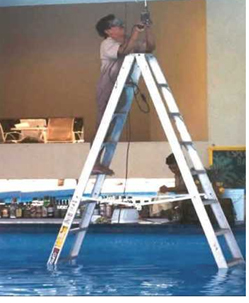 workman repairing or installing electrical equipment while standing on a metal ladder immersed in a swimming pool