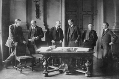 Photo of six German delegates standing around a large table that has several stacks of papers.
